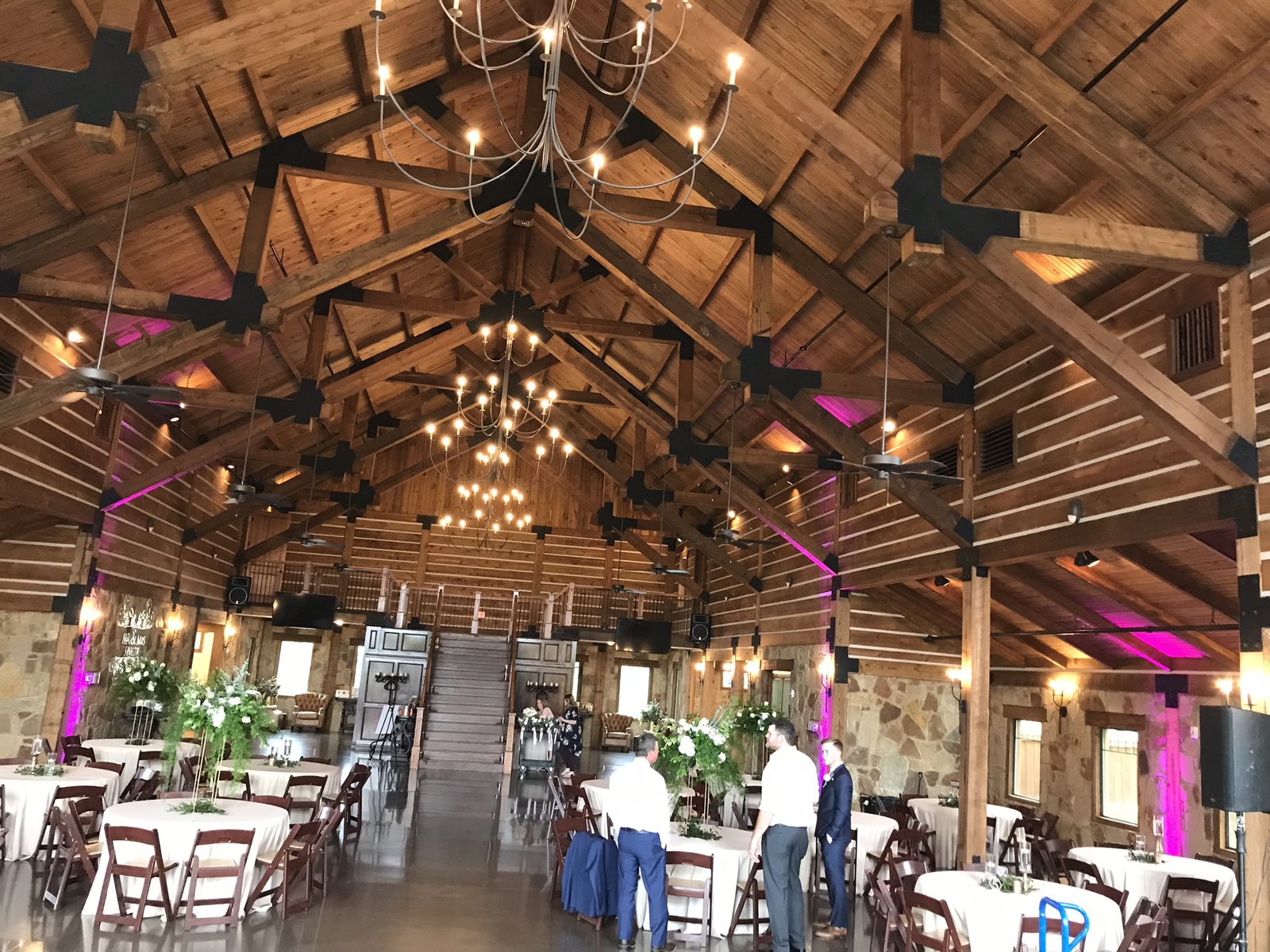 Magenta uplighting on the stone and timber walls of a barn hall with guests at round tables