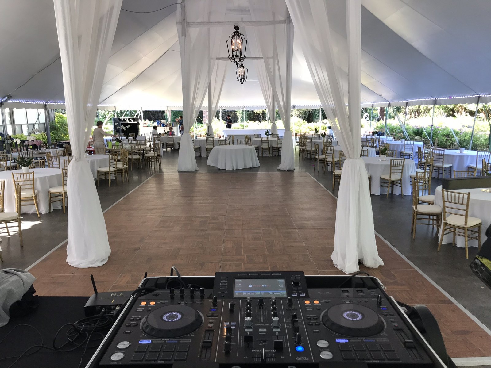 A DJ controller set at the end of a dance floor inside a draped tent reception